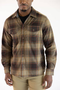 A man wearing a long-sleeve button-up plaid flannel shirt in brown, beige, and black, paired with khaki pants, against a plain white background.