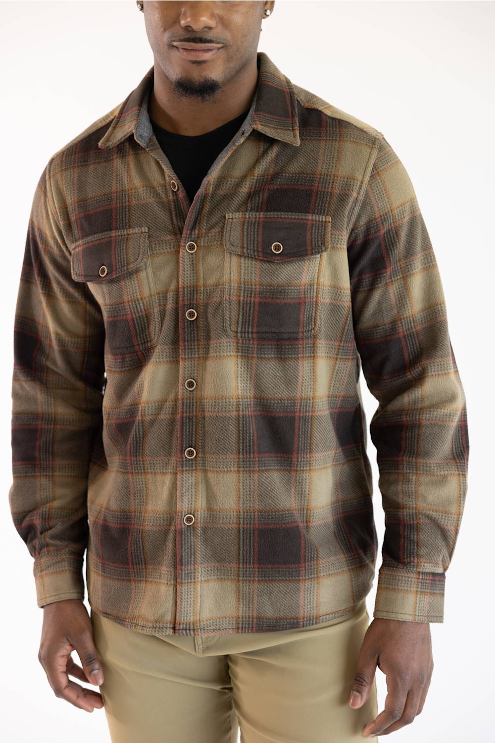 A man wearing a long-sleeve button-up plaid flannel shirt in brown, beige, and black, paired with khaki pants, against a plain white background.