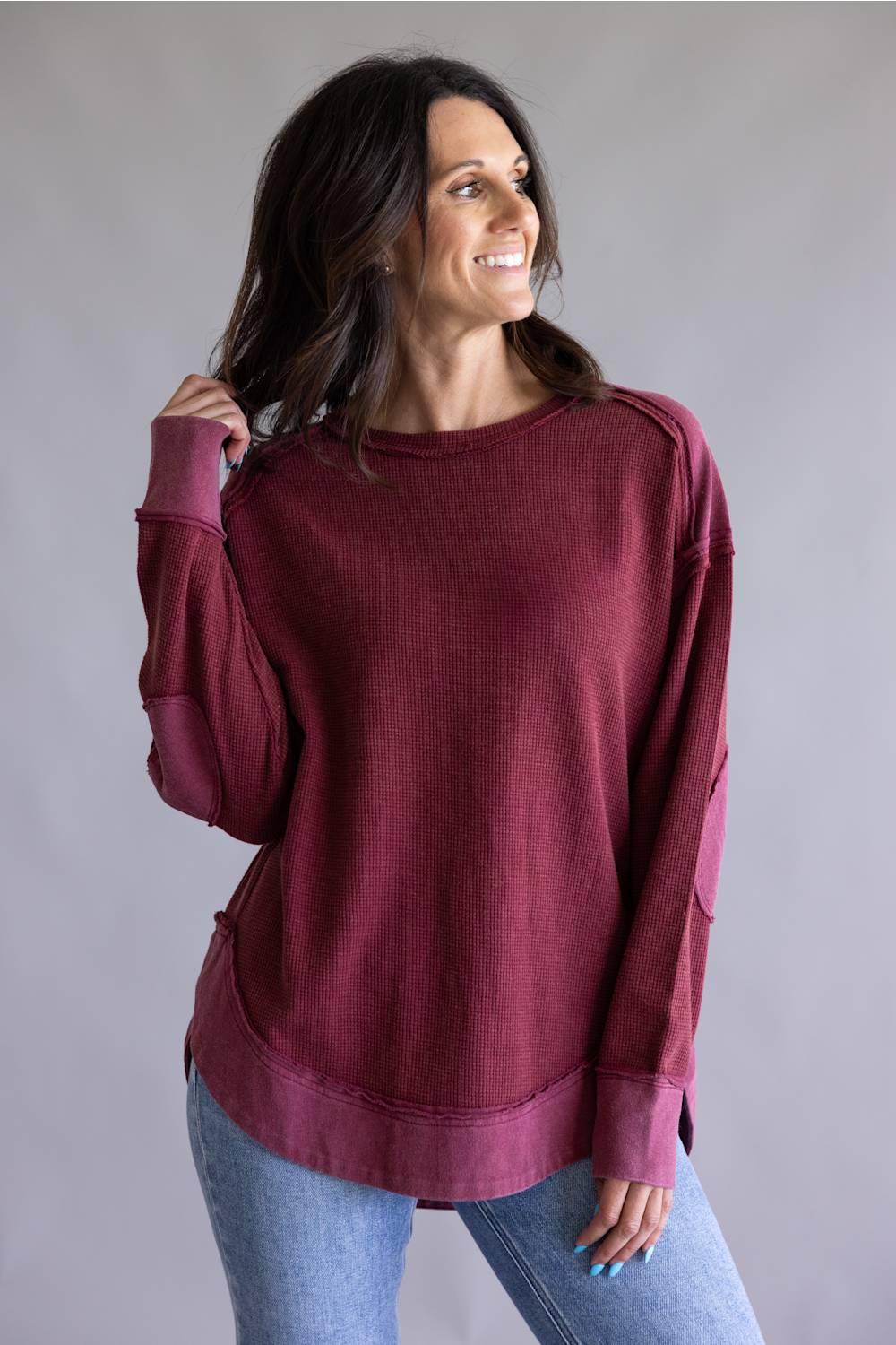 Woman wearing a burgundy sweatshirt and blue jeans against a gray background
