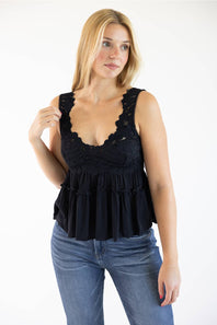 A woman modeling a black sleeveless ruffled top with scalloped lace trim and a tiered peplum, paired with blue jeans, against a plain white background.