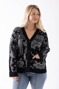 A blonde woman wearing a black knit cardigan with a white abstract pattern, paired with blue jeans, photographed against a plain white background.