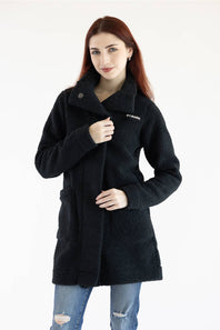 A woman with red hair wearing a black textured teddy coat and blue jeans, standing against a plain white studio background. The brand name 'COLUMBIA' is visible on the left chest of the coat.