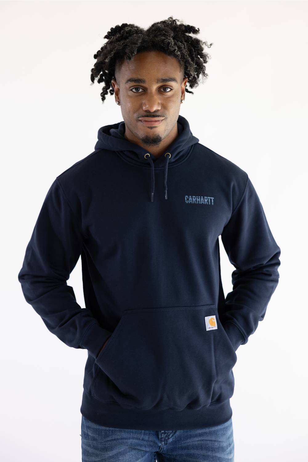 A man wearing a navy blue Carhartt pullover hoodie with the brand name printed in light blue on the left chest and the signature Carhartt patch on the front pocket, set against a plain white background.