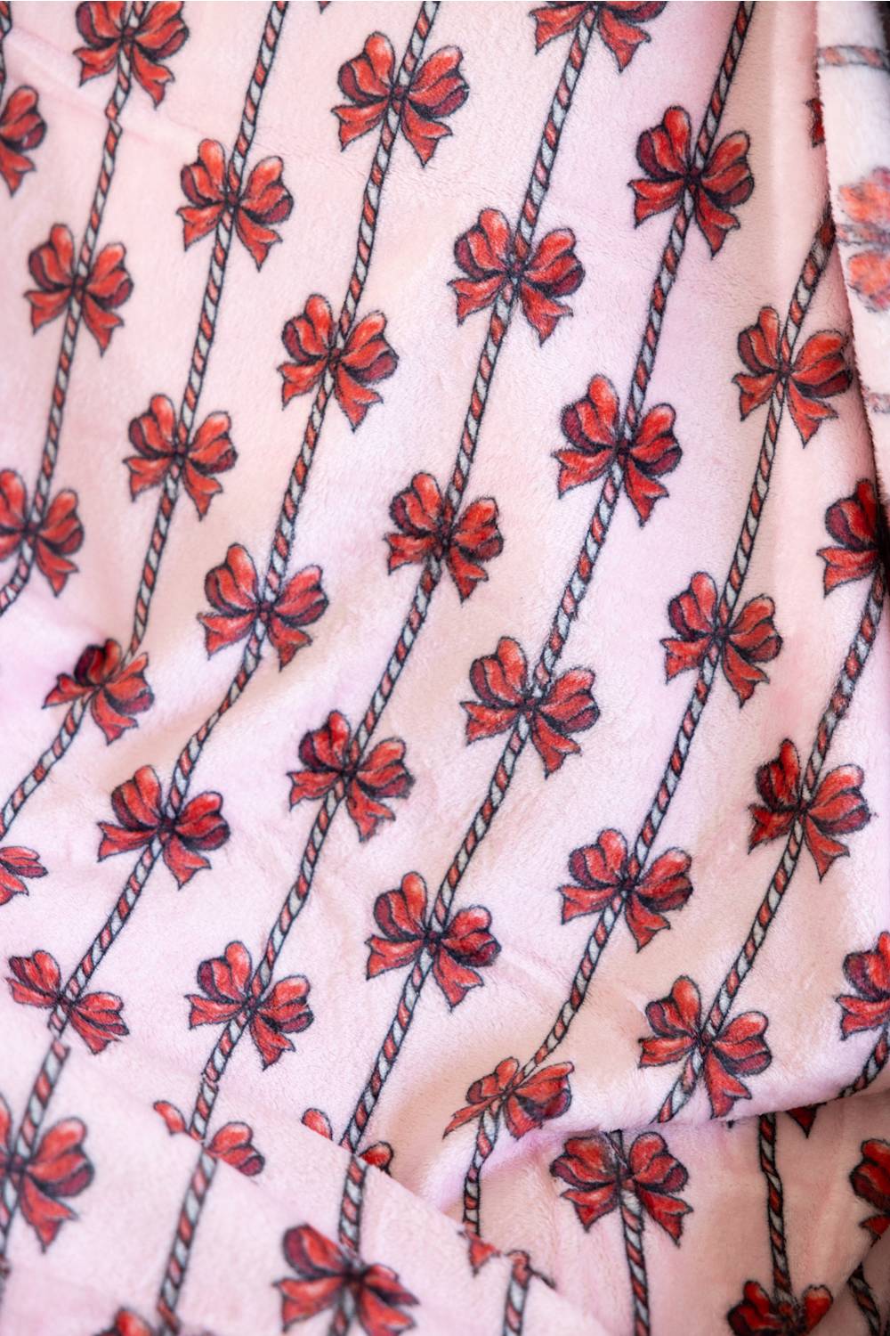 A close-up of a light pink blanket with a repeating pattern of red and black bow motifs arranged diagonally.