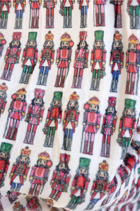 A close-up of a blanket with an all-over repeating print of colorful nutcracker figures in red, green, blue, and gold.