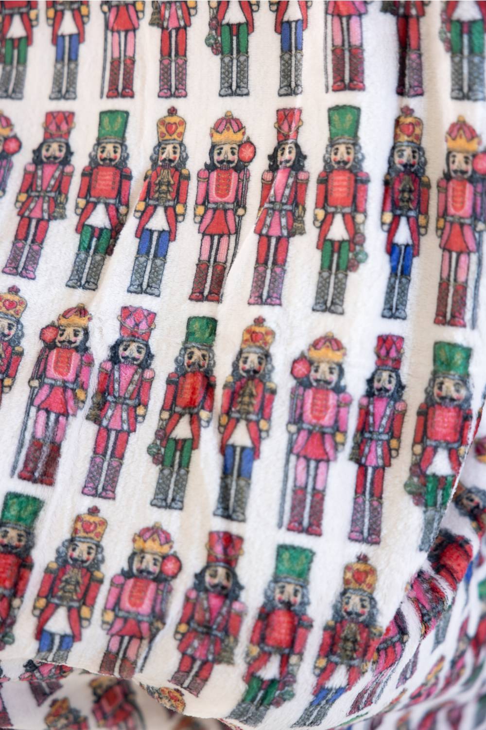 A close-up of a blanket with an all-over repeating print of colorful nutcracker figures in red, green, blue, and gold.