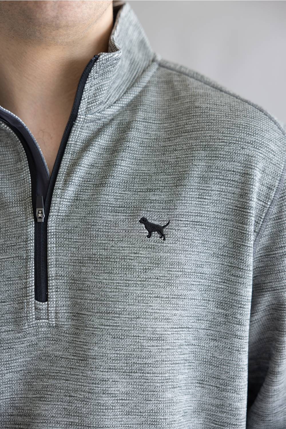 Close-up of a person wearing a heather gray quarter-zip pullover with a small black cat logo on the left chest.