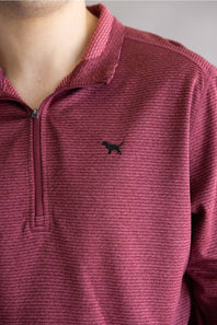 A close-up of a person wearing a textured, heathered magenta-burgundy quarter-zip pullover with a small black dog silhouette logo on the left chest.