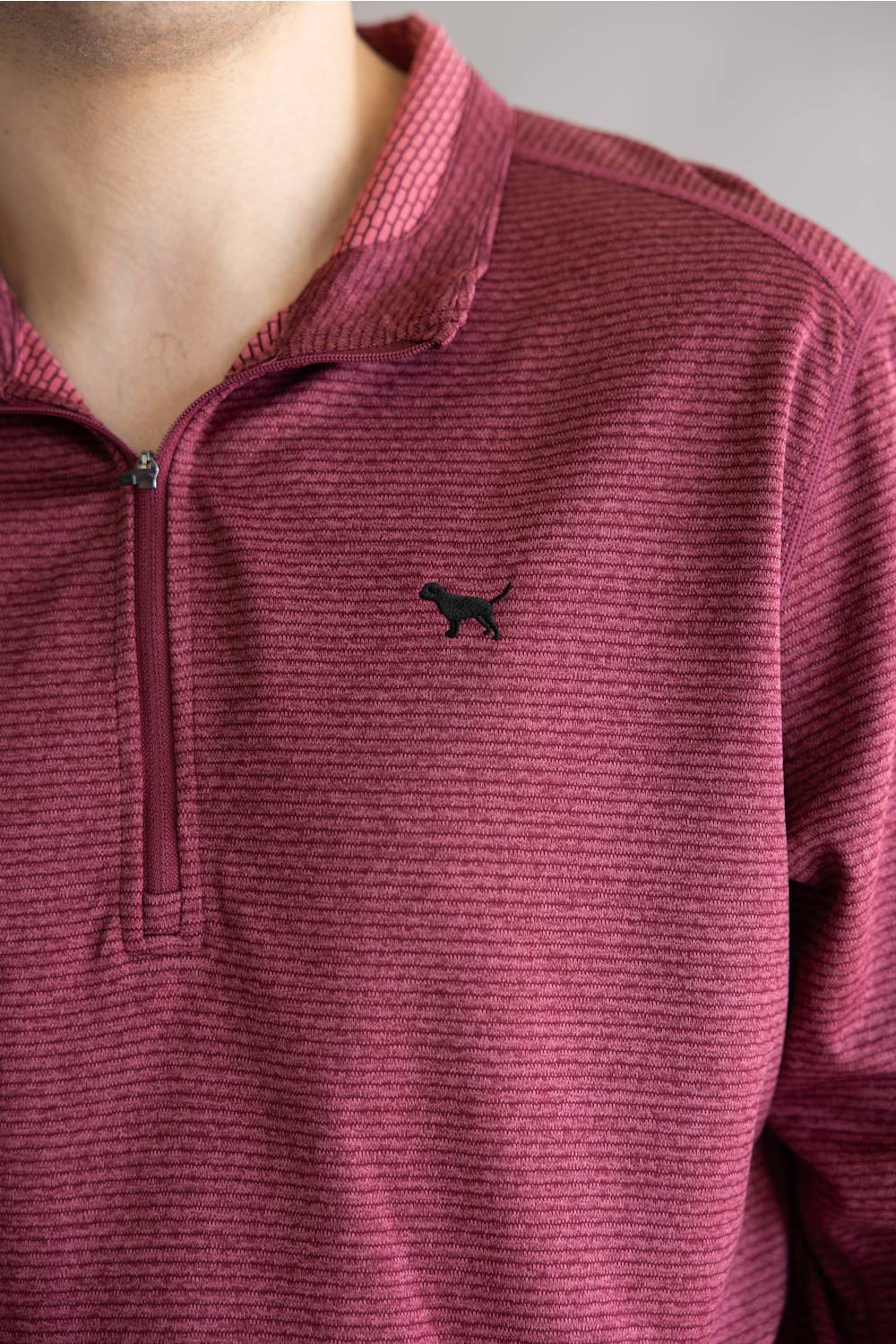 A close-up of a person wearing a textured, heathered magenta-burgundy quarter-zip pullover with a small black dog silhouette logo on the left chest.