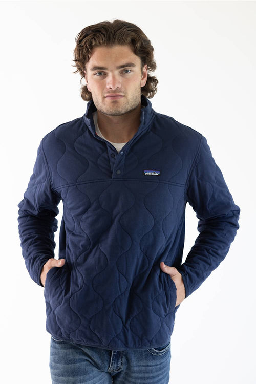 A man wearing a navy blue Patagonia quilted pullover jacket with a stand collar and zippered chest pocket, paired with blue jeans, against a plain white studio background.