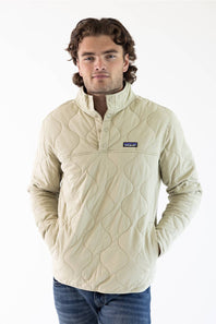 A man wearing an off white Patagonia quilted pullover jacket with a stand collar and zippered chest pocket, paired with blue jeans, against a plain white studio background.
