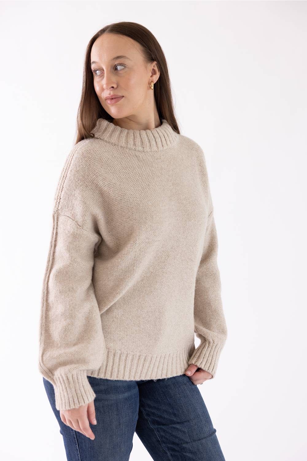A woman modeling the Pink Rose Mock Neck Sweater in Heather Oatmeal, featuring a ribbed mock neck, drop shoulders, and long sleeves with ribbed cuffs, paired with dark-wash jeans.