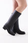 A pair of black knee-high leather boots worn on a model's legs, shown from a side profile against a clean white background.