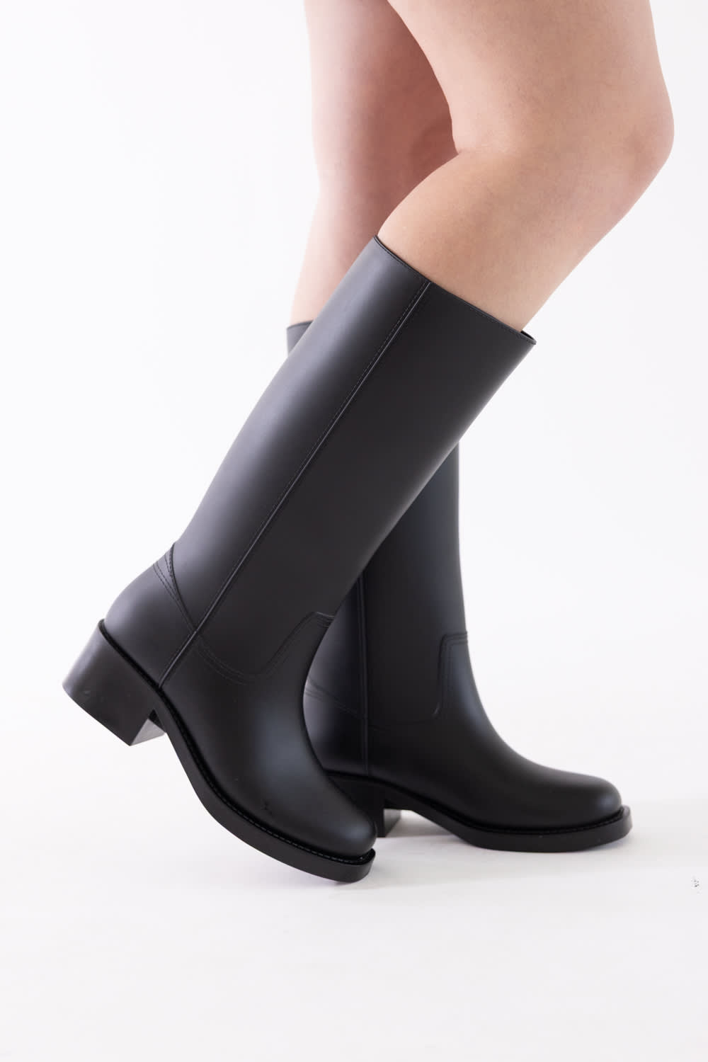 A pair of black knee-high leather boots worn on a model's legs, shown from a side profile against a clean white background.