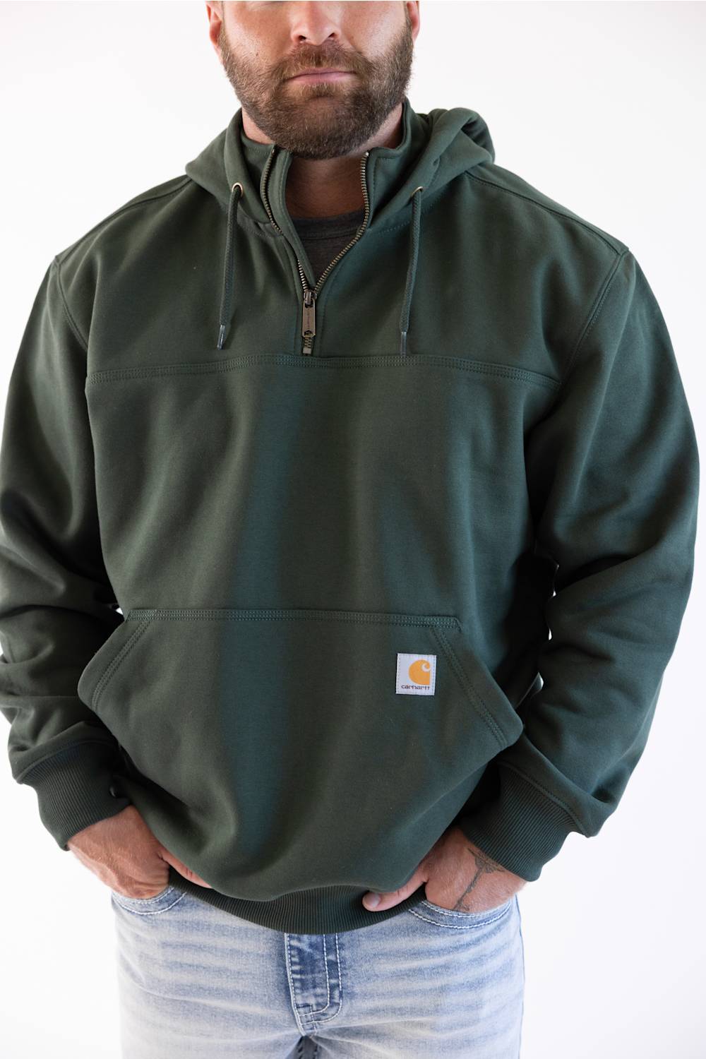 Model wearing a men's dark green forestry hoodie with hands in front pockets paired with light wash denim jeans.