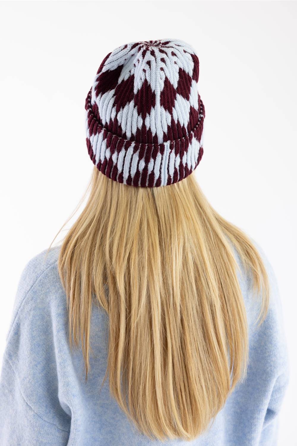 A person viewed from behind wearing a knit beanie with a burgundy and white diamond pattern, paired with a light blue-gray sweatshirt against a plain white background.
