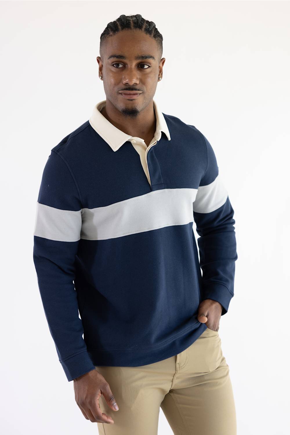 A man wearing a navy and grey color-blocked long-sleeve rugby shirt with blue jeans, standing against a plain light background.