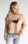 A woman wearing a beige knit sweater with a dachshund graphic wearing a burgundy polka-dot sweater, paired with light gray jeans, against a plain light gray background.