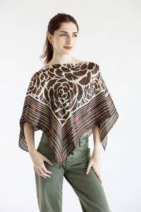 A woman modeling a brown and beige floral-patterned shawl poncho over olive green pants, photographed against a plain white studio background.