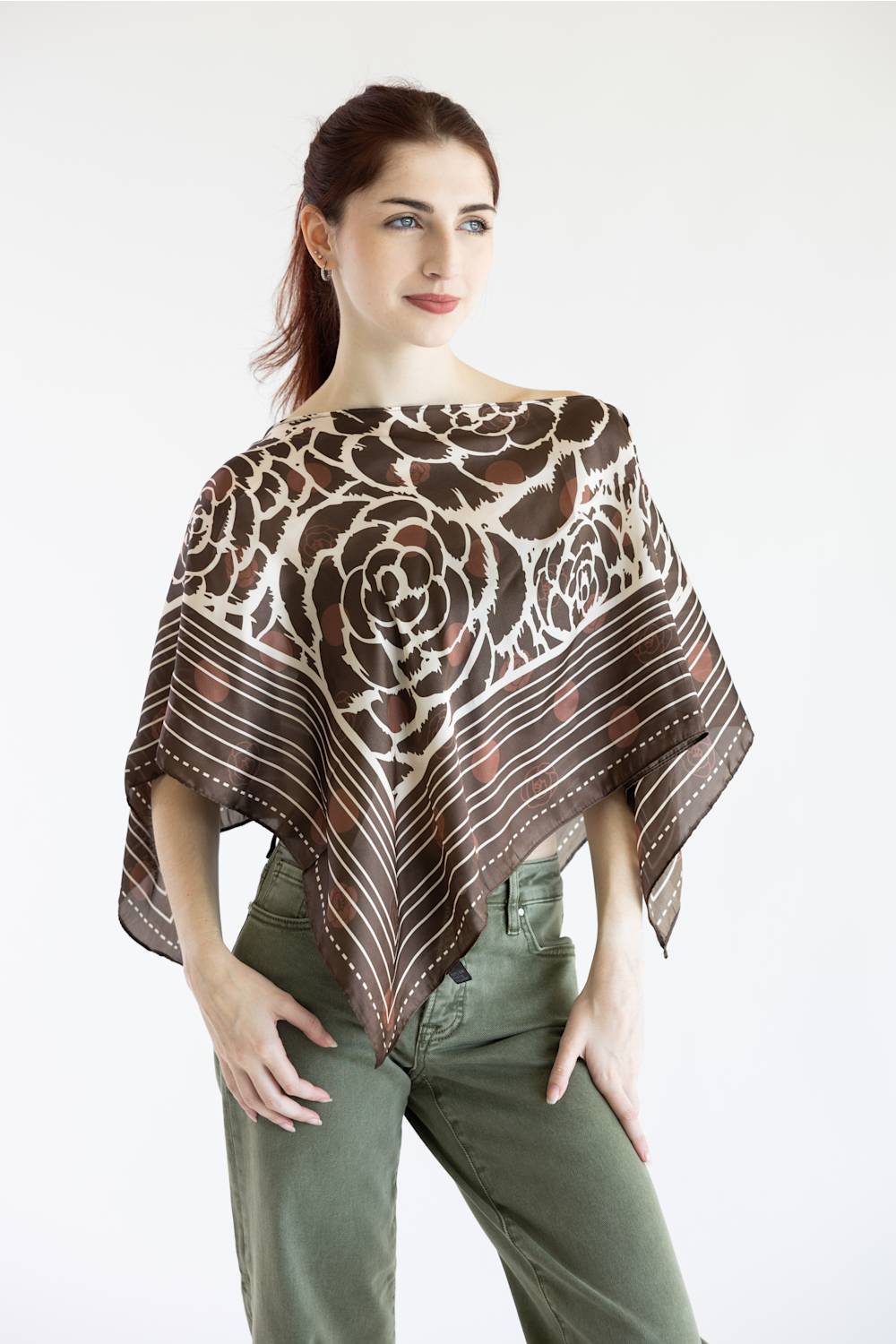 A woman modeling a brown and beige floral-patterned shawl poncho over olive green pants, photographed against a plain white studio background.