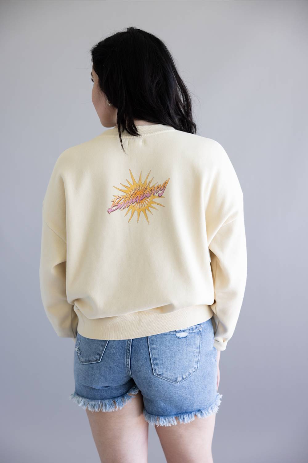 Person wearing a light-colored sweatshirt with a graphic design on the back, standing against a plain background.