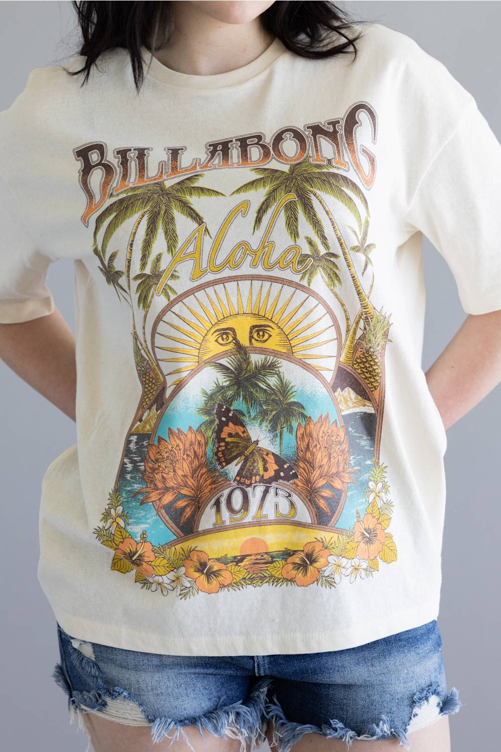 Person wearing a 'Billabong Aloha' t-shirt with tropical graphics on a plain background
