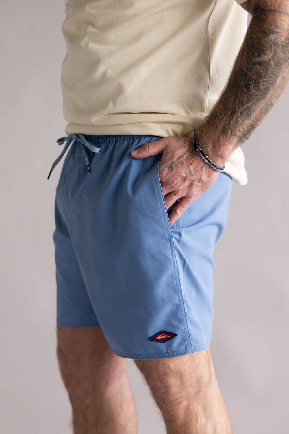 Side view of a person wearing light blue shorts with a small logo on a plain background. The shorts are the Quiksilver Saltwater Volley 17" Swim Trunks for Men in Riviera