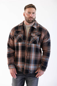 The model is standing facing forward with his hands in his pockets, wearing the sherpa-lined flannel shacket over a neutral crewneck shirt, paired with dark wash jeans and white sneakers.
