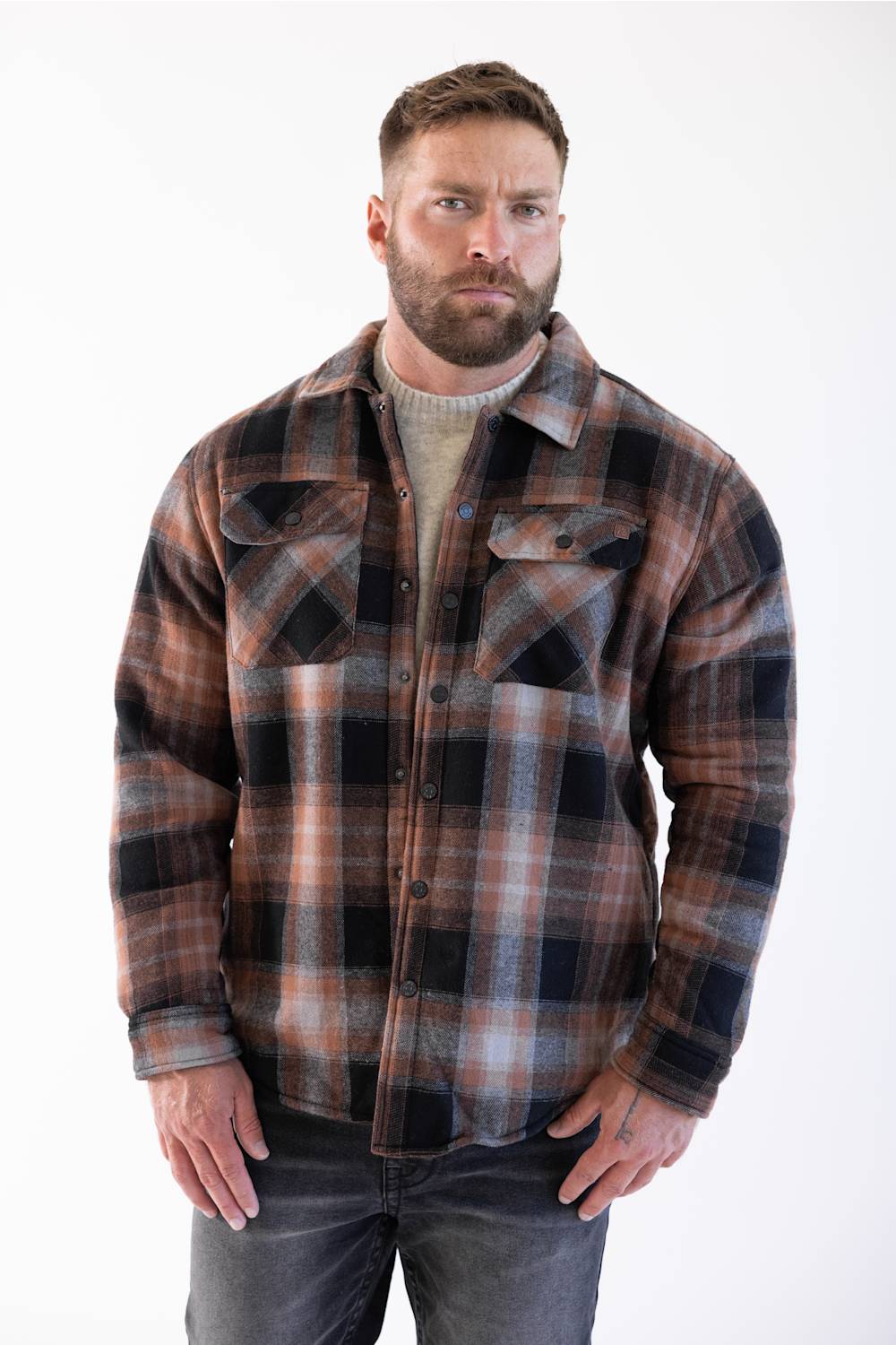 The model is standing facing forward with his hands in his pockets, wearing the sherpa-lined flannel shacket over a neutral crewneck shirt, paired with dark wash jeans and white sneakers.