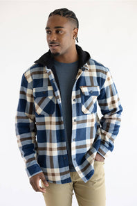 A man wearing a blue, brown, and beige plaid hooded flannel shirt over a dark gray t-shirt and khaki pants, photographed against a plain white studio background.