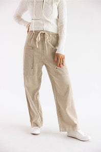 A person wearing beige wide-leg cargo-style pants with a drawstring waist, paired with a white ribbed sweater and white sneakers, photographed against a clean white studio background.