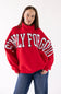 A woman wearing a bright red sweatshirt with 'SIMPLY FOR GOOD' printed in white arched letters across the chest, paired with blue jeans, against a plain white studio background.