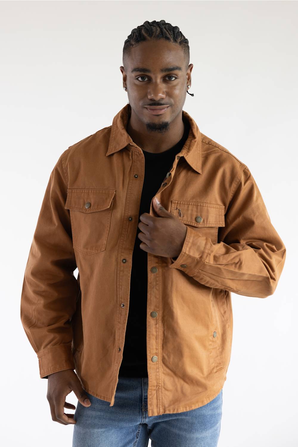 A man wearing a brown button-up overshirt jacket over a black t-shirt and blue jeans, photographed against a plain white studio background.