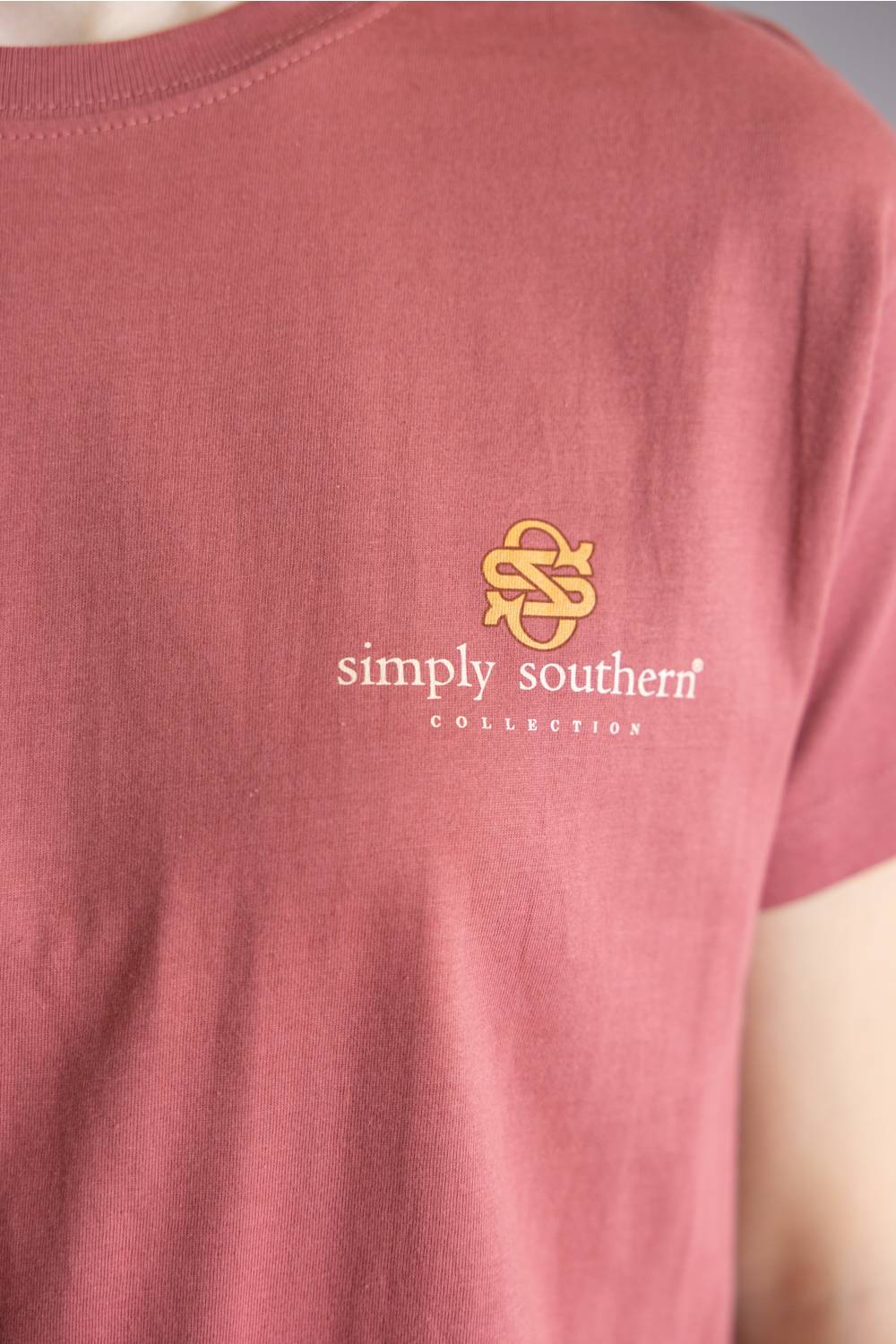 A dusty rose short-sleeve t-shirt with a graphic of a cow, rooster, and sheep on the front, layered over a second view of the same shirt showing a small chest logo.