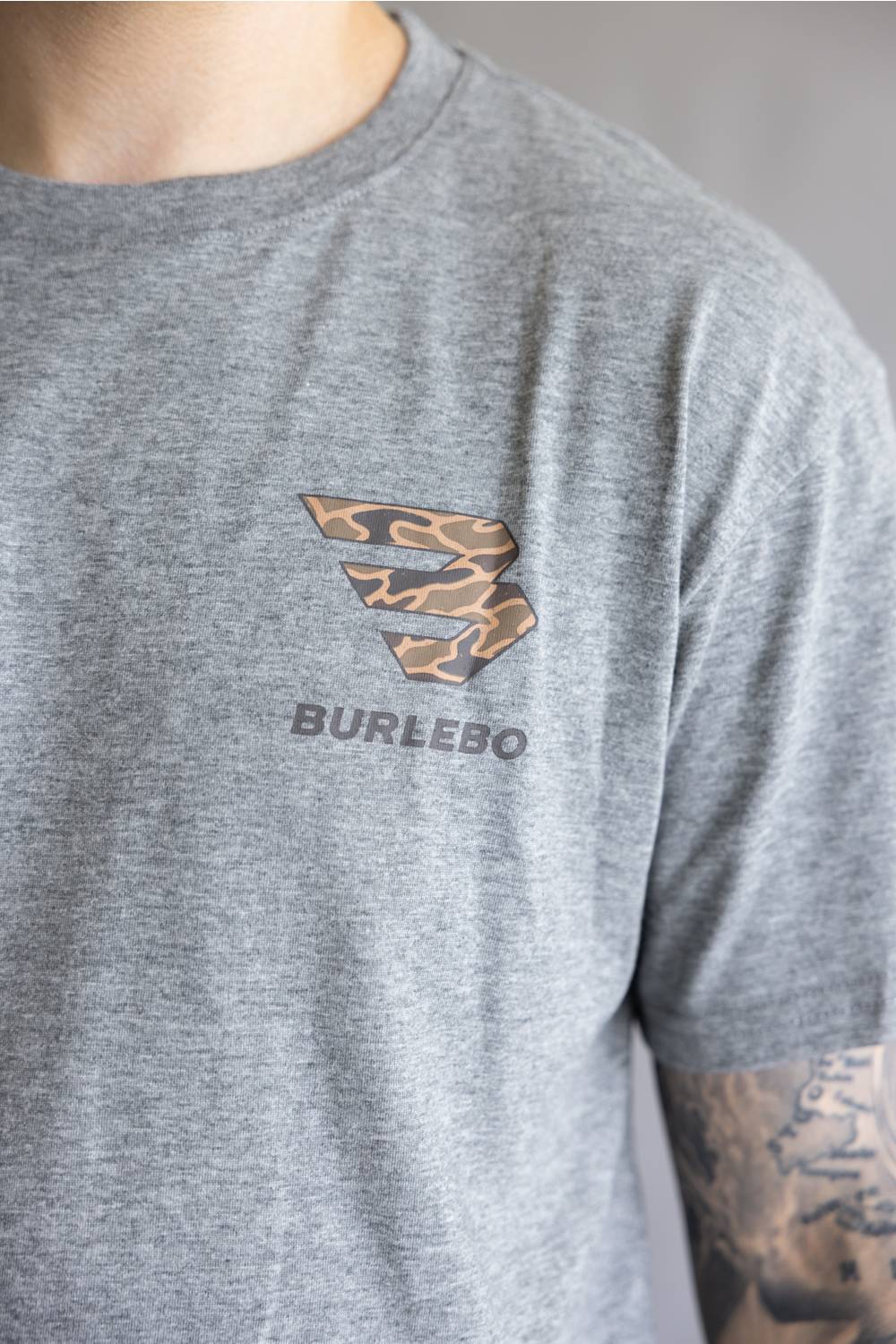 A close-up of a person wearing a heather gray t-shirt with a Burlebo brand logo printed on the chest in a leopard print pattern.