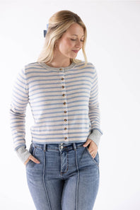 A woman wearing a cream and light blue horizontally striped button-up cardigan sweater with brown buttons, paired with blue jeans, against a plain white studio background.