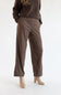 A person wearing brown wide-leg pants with thin beige horizontal stripes, paired with a dark brown sweater and beige heeled shoes, photographed against a plain white studio background.