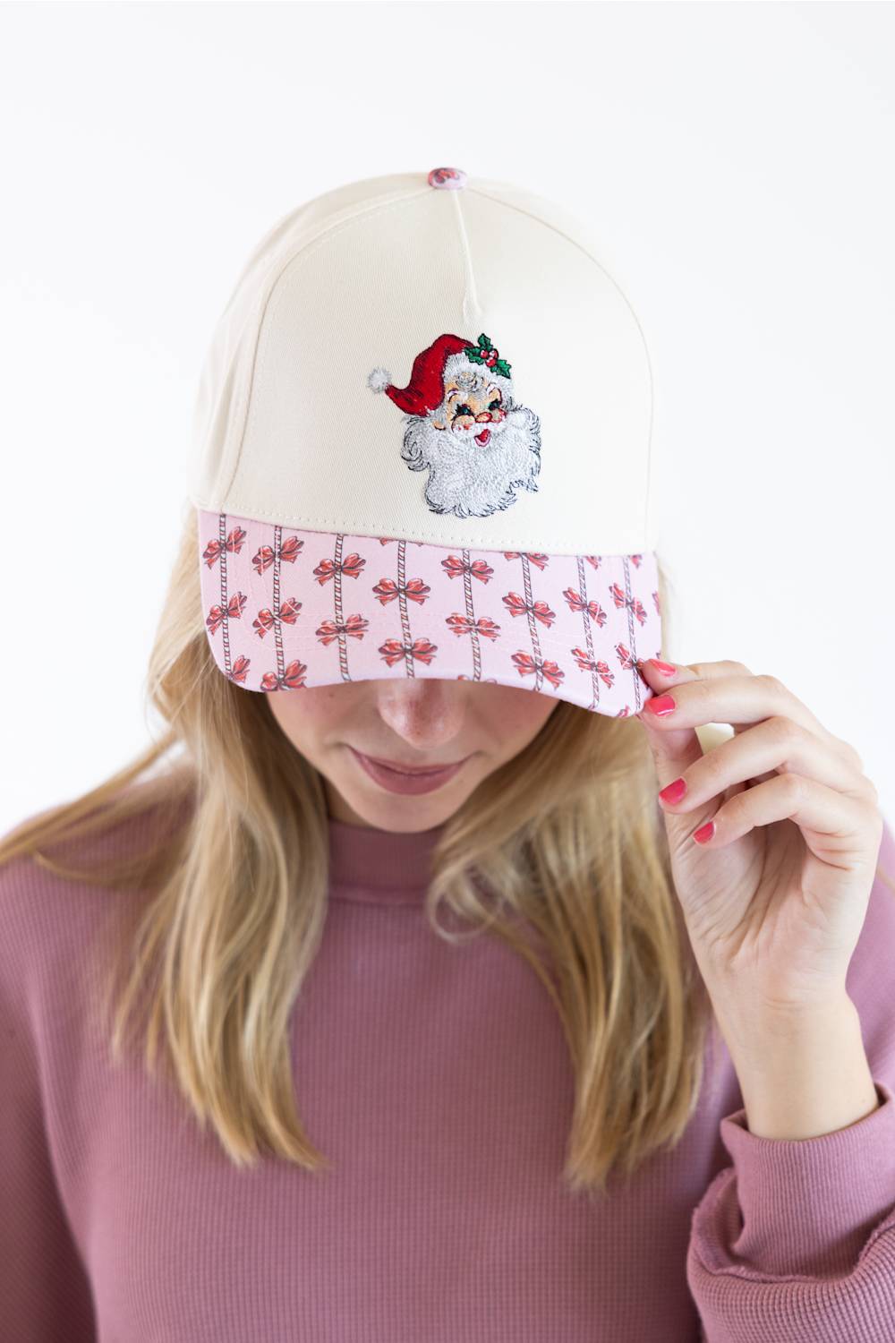 Model wearing the Simply Southern Classic Santa Holiday Hat for Women in Cream and Red, featuring an embroidered vintage Santa Claus patch on the cream front, a pink patterned brim with red bows and candy canes, paired with a dusty pink sweatshirt.