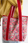 A red and pink patterned tote bag with dog illustrations, worn over the shoulder of a person wearing a yellow sweatshirt.