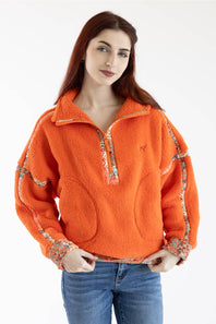 A woman wearing a bright orange sherpa fleece half-zip pullover with floral patterned trim on the sleeves and collar, paired with blue jeans, against a plain white background.