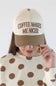 A woman wearing a cream and tan trucker hat with the embroidered text 'COFFEE MAKES ME NICER' in brown, paired with a cream long-sleeve top with brown polka dots, against a plain light gray background.