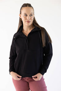 A woman modeling a black long-sleeve quarter-zip pullover jacket with a zip collar, paired with dusty rose pants, against a plain white studio background.
