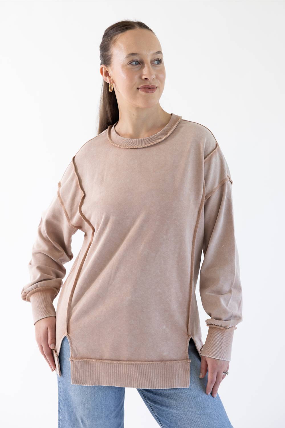 A woman modeling a dusty rose long-sleeve crewneck sweatshirt with unique ragged sleeve edges and side slits, paired with blue jeans against a plain white background.
