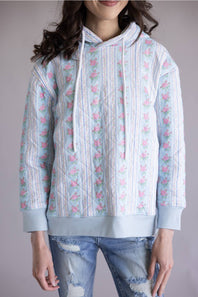 Simply Southern Quilted Hoodie for Women in Rose Stripe; Person wearing a light blue hoodie with floral patterns on a plain background