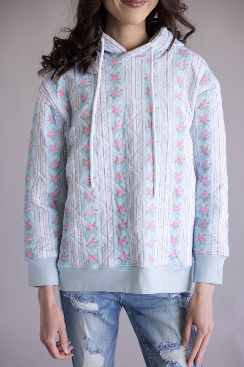 Simply Southern Quilted Hoodie for Women in Rose Stripe; Person wearing a light blue hoodie with floral patterns on a plain background