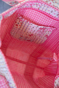 Close-up view of a pink and red gingham fabric bag interior with a floral patterned pocket lining.