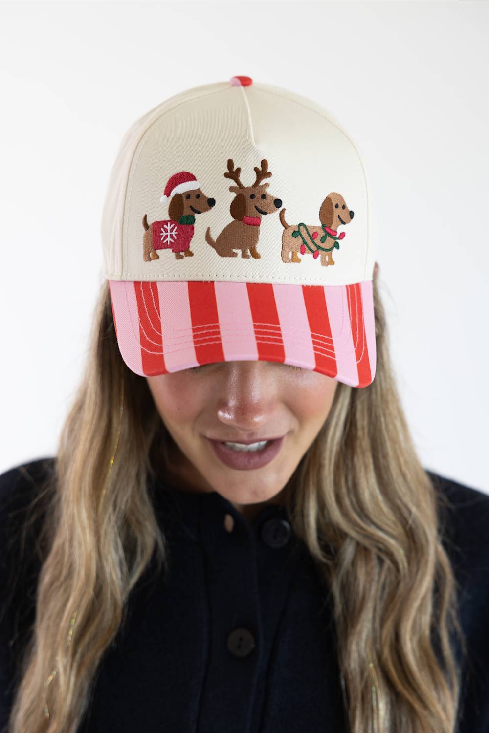 Model wearing the Simply Southern Santa Dogs Holiday Hat for Women in Cream and Red/Pink Stripe, featuring three embroidered dachshunds in holiday attire on the cream front panel and a red and pink striped visor.