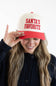 Model holding the brim of the Simply Southern Santa’s Favorite Holiday Hat for Women in Cream/Red, featuring red embroidered collegiate-style lettering reading “SANTA’S FAVORITE” on the cream front panel and a solid red visor, paired with a dark button-down cardigan.