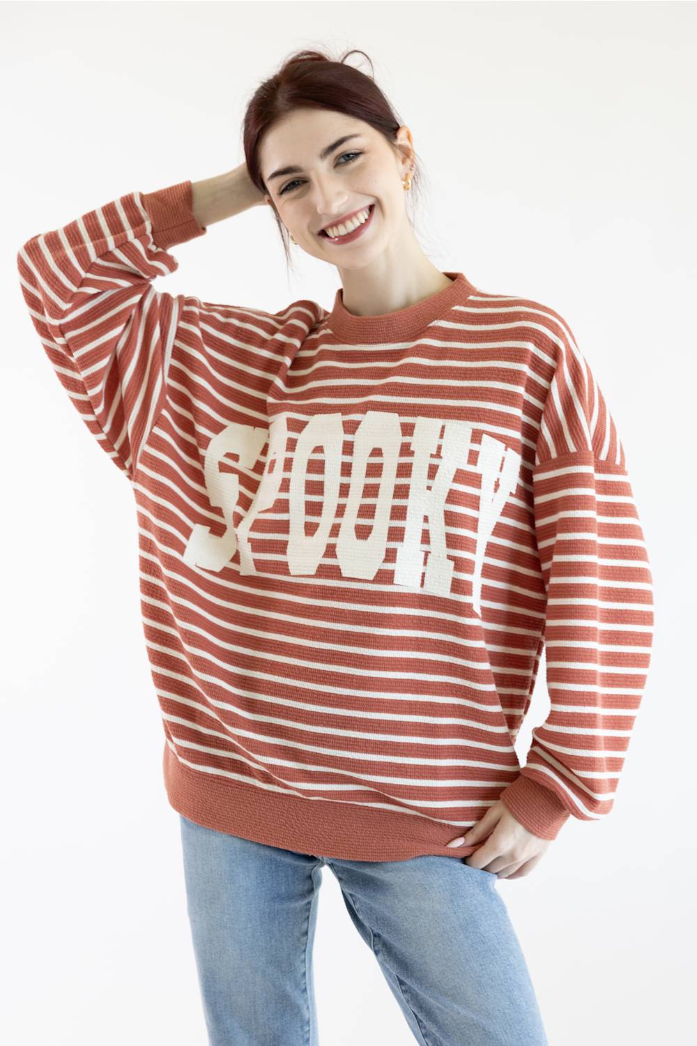 Women wearing dusty mauve sweatshirt with white horizontal stripes, SPOOKY screen printed on front and blue denim jeans on a basic background