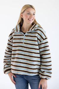A woman wearing a fuzzy quarter-zip pullover sweater with horizontal brown, light blue, and cream stripes, paired with blue jeans, against a plain white background.
